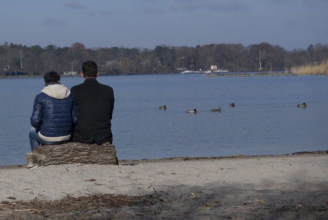 27 March 2022, Berlin: Two men sit by the Havel River and enjoy the spring-like weather. Photo: Paul Zinken\/dpa