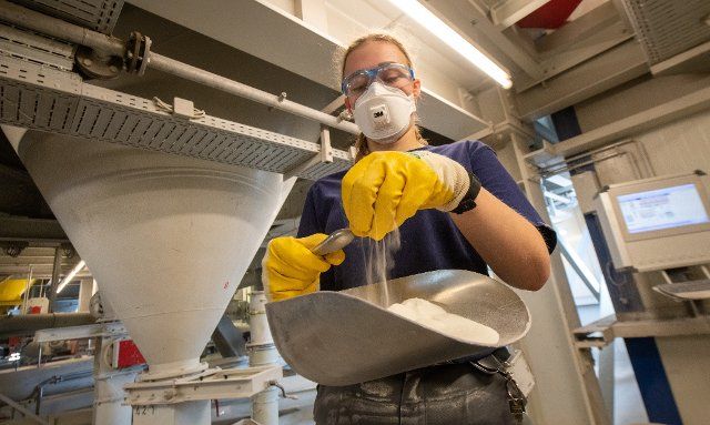 20 April 2022, Baden-Wuerttemberg, Ulm: Cora Kuttmann, a chemical technician, lets a powder trickle through her hand into a chute at Uzin Utz. The listed building materials producer presents the company\