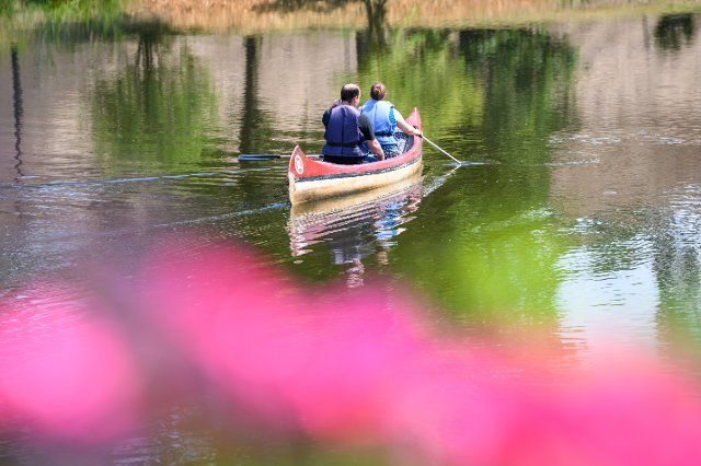 25 June 2022, Hamburg: A man and a woman paddle in a canoe across the lake at the Wilhelmsburg community center. Photo: Jonas Walzberg\/dpa