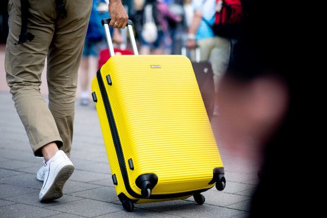 25 June 2022, Lower Saxony, Norddeich: A man walks to the ferry terminal in the harbor with his yellow suitcase to travel to the island of Norderney. North Rhine-Westphalia is the first German state to start its summer vacation. Photo: Hauke-Christian Dittrich\/dpa