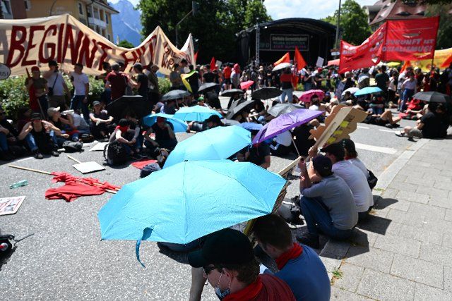 26 June 2022, Bavaria, Garmisch-Partenkirchen: Participants of a large demonstration of the alliance "Stop G7 Elmau" protect themselves with umbrellas against the heat. Germany is hosting the G7 summit of economically strong democracies from June 26 to 28, 2022. Photo: Angelika Warmuth\/dpa