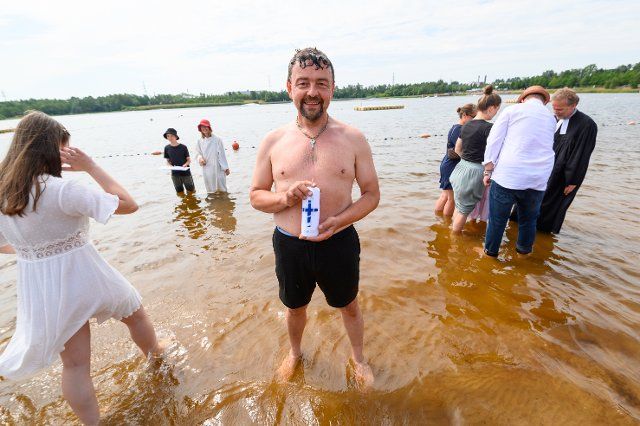 26 June 2022, Schleswig-Holstein, Norderstedt: Baptized Mirko Hein (49), stands with a baptismal candle in the Stadtparksee after his baptism. A mass baptism with 57 participants and around 500 guests was celebrated by seven church congregations at and in the Stadtparksee in Norderstedt near Hamburg. Photo: Jonas Walzberg\/dpa