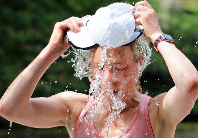 26 June 2022, Hamburg, Au··enalster: Half marathon, Hamburg. A participant fills her cap with water at a refreshment station and tips it over her head. Once again, participants and organizers had to contend with high temperatures at the largest half marathon in Hamburg. (to "Hamburg half marathon: This time, fewer aid missions due to heat") Photo: Markus Tischler\/dpa