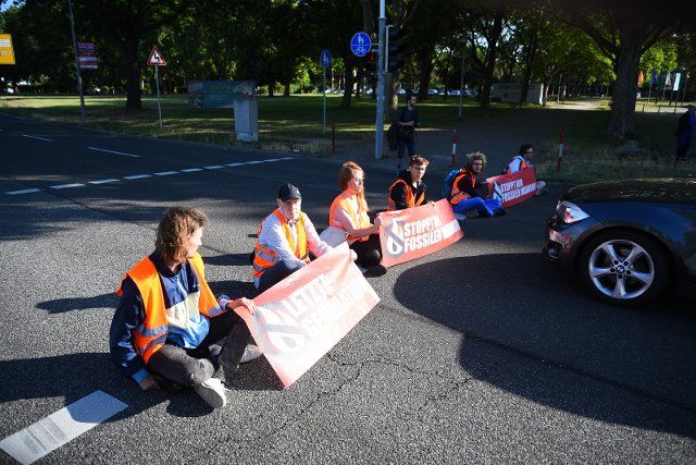 13 June 2022, Baden-Wuerttemberg, Mannheim: Activists from the group "Last Generation" sit on a street during a blockade. A banner reads: "Stop the fossil madness". Photo: René Priebe\/dpa