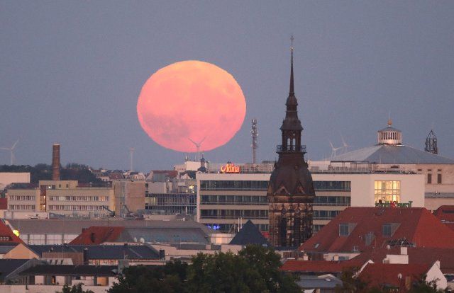11 August 2022, Saxony, Leipzig: The moon rises behind the city center. Photo: Sebastian Willnow\/dpa