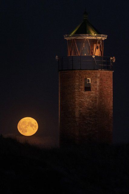 11 August 2022, Schleswig-Holstein, Kampen: The full moon rises behind the lighthouse Quermarkenfeuer Rotes Kliff on the North Sea island of Sylt. Photo: Swen Pförtner\/dpa