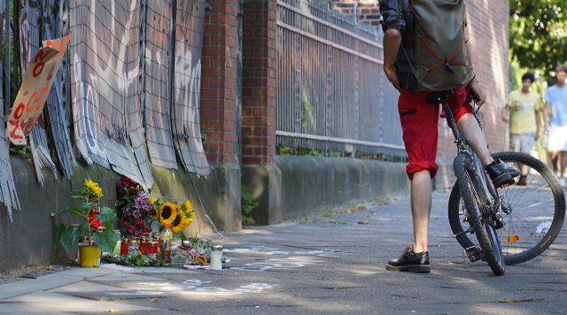 12 August 2022, North Rhine-Westphalia, Dortmund: A bicyclist stopped at a fence commemorating a teenager shot by police with candles and flowers. The 16-year-old was hit by five shots from a police submachine gun in the area behind. (to dpa: "Sympathy at funeral service for teenager shot by police") Photo: Gregor Bauernfeind\/dpa