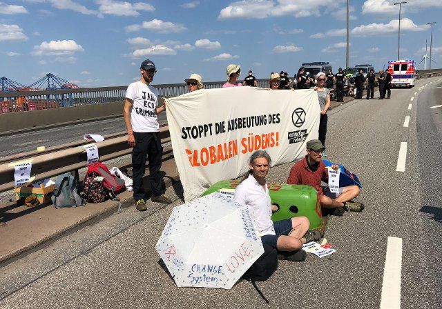 13 August 2022, Hamburg: Climate activists sit at a demonstration on the Köhlbrand Bridge holding a banner "Stop the exploitation of the global south!". Photo: Daniel Bockwoldt\/dpa