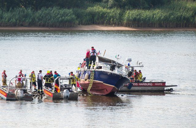 14 August 2022, Hamburg: Emergency personnel with boats work on a pleasure boat on the Elbe near Altengamme. The boat, manned by three people, had veered off course in the morning and hit the rocky shore. Photo: Daniel Bockwoldt\/dpa