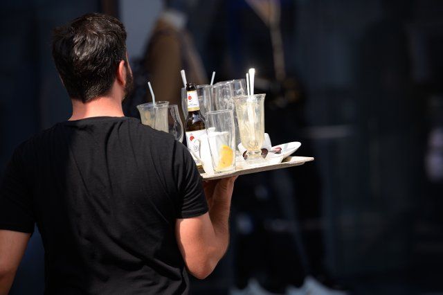 16 August 2022, Hamburg: A waiter at the Alsterarkaden carries a tray with used glasses and empty bottles. Photo: Jonas Walzberg\/dpa