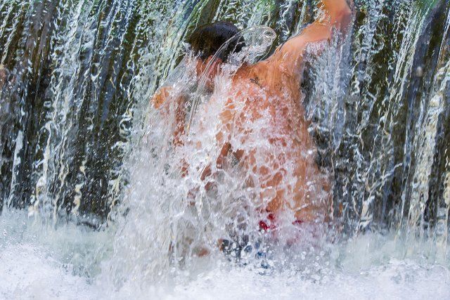16 August 2022, Bavaria, Munich: A young man cools off under an artificial waterfall of the Eisbach in the English Garden. Photo: Peter Kneffel\/dpa