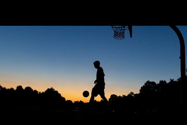 16 August 2022, Bavaria, Nuremberg: A youth plays basketball at a public hoop under a bridge at dusk. Photo: Daniel Karmann\/dpa