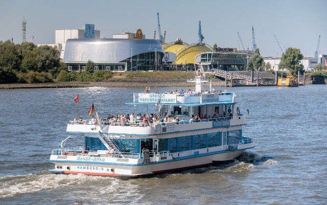 15 August 2022, Hamburg: The harbor cruise ship "Hanse Star" sails down the Elbe past the Stage Theater buildings. Photo: Markus Scholz\/dpa\/picture alliance\/dpa | Markus Scholz
