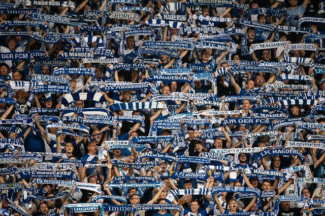 19 August 2022, Saxony-Anhalt, Magdeburg: Soccer: 2nd Bundesliga, 1. FC Magdeburg - Hannover 96, Matchday 5, MDCC Arena. Magdeburg fans are in the stands with scarves. Photo: Swen Pförtner\/dpa - IMPORTANT NOTE: In accordance with the requirements of the DFL Deutsche Fußball Liga and the DFB Deutscher Fußball-Bund, it is prohibited to use or have used photographs taken in the stadium and\/or of the match in the form of sequence pictures and\/or video-like photo series