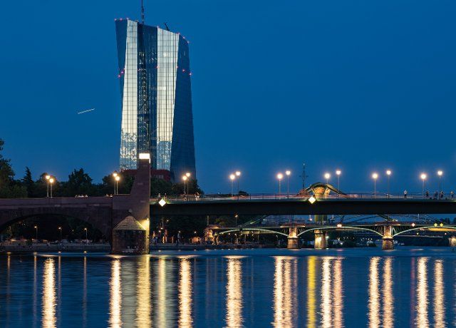19 August 2022, Hessen, Frankfurt\/Main: The headquarters of the European Central Bank (ECB) reflects the last evening light over the illuminated Main bridges. (Shot with longer exposure time) Photo: Frank Rumpenhorst\/dpa