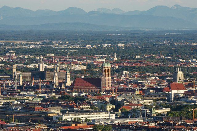10 August 2022, Bavaria, Munich: View from the Olympiaberg to the Munich city center with the Frauenkirche. In the background you can see the mountains of the Alps. Photo: Soeren Stache\/dpa