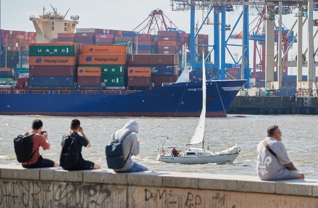 03 September 2022, Hamburg: People enjoy the sun and the view of the container port on the Elbe beach in Övelgönne while a sailboat passes downstream. Photo: Georg Wendt\/dpa