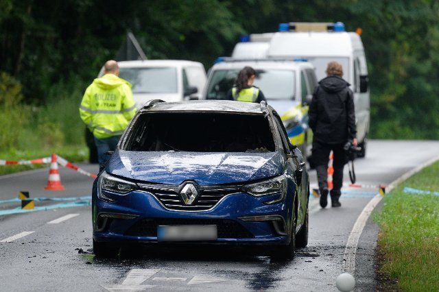 22 July 2022, North Rhine-Westphalia, Cologne: A burnt-out car stands at the scene after a cash-in-transit robbery. Several masked men attacked and shot at an armored car in Cologne. Photo: Henning Kaiser\/dpa - ATTENTION: License plate(s) have been pixelated for legal reasons