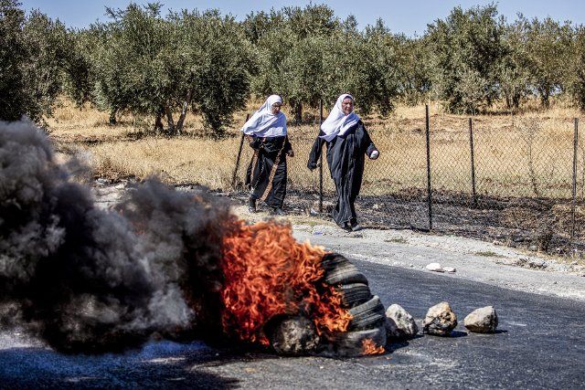 30 September 2022, Palestinian Territories, Bethlehem: Two Palestinian women walk next to a burning tires during a protest following the funeral of the 7 years old Rayan Suleiman. Rayan died after being chased by Israeli forces in Tekoa town. Photo: Ilia Yefimovich\/dpa