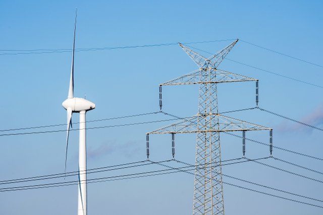 30 September 2022, Lower Saxony, Elsfleth: A wind turbine stands next to a high-voltage power line in sunny autumn weather, spinning in the wind. Photo: Hauke-Christian Dittrich\/dpa