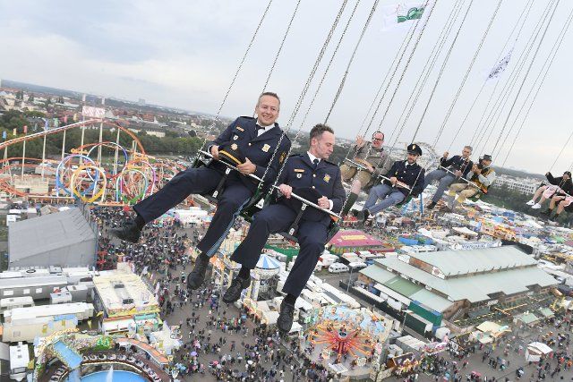 25 September 2022, Bavaria, Munich: The head of the Wiesnwache, Polizeioberrat Christian Schäfer (l) and Artur Mitterer (r) first police chief inspector, ride a giant chain carousel during the presentation of the Italian and French police officers at the Oktoberfest. The Wiesn will take place from September 17 to October 3, 2022. Photo: Felix Hörhager\/dpa