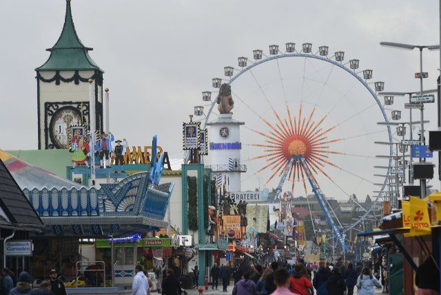 26 September 2022, Bavaria, Munich: Visitors to the Wiesn walk in front of the Ferris wheel across the Theresienwiese at the Oktoberfest. The Wiesn will take place from September 17 to October 3, 2022. Photo: Felix Hörhager\/dpa