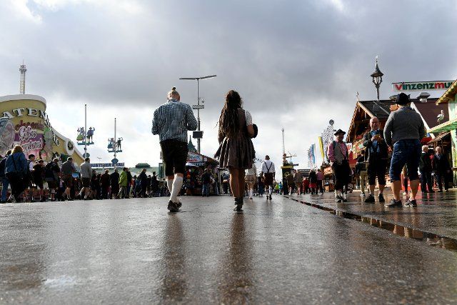 26 September 2022, Bavaria, Munich: Visitors to the Wiesn walk across the Theresienwiese at the Oktoberfest under dark clouds. The Wiesn takes place from September 17 to October 3, 2022. Photo: Felix Hörhager\/dpa