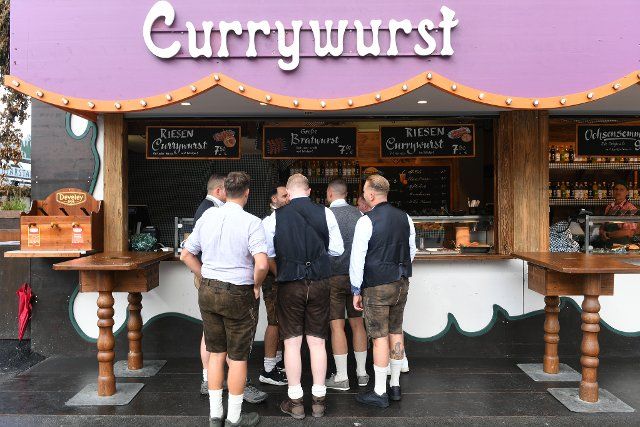 26 September 2022, Bavaria, Munich: Visitors to the Oktoberfest stand in front of a curry sausage stand on the Theresienwiese. The Wiesn takes place from September 17 to October 3, 2022. Photo: Felix Hörhager\/dpa