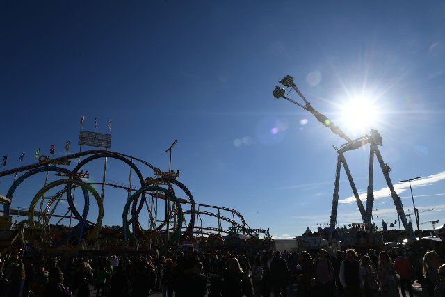 26 September 2022, Bavaria, Munich: The sun shines under a blue sky behind a ride and the five-looping roller coaster. The Wiesn takes place from September 17 to October 3, 2022. Photo: Felix Hörhager\/dpa