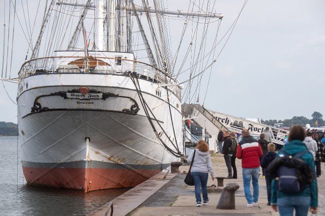 05 October 2022, Mecklenburg-Western Pomerania, Stralsund: Tourists walk in front of the sailing ship "Gorch Fock" (I) in the city harbor in sunny weather. The ship, built in 1933, went to the Soviet Union as a reparation in 1951 and was christened "Towarishch" ("Comrade"). Since 2003 it has been moored in Stralsund\