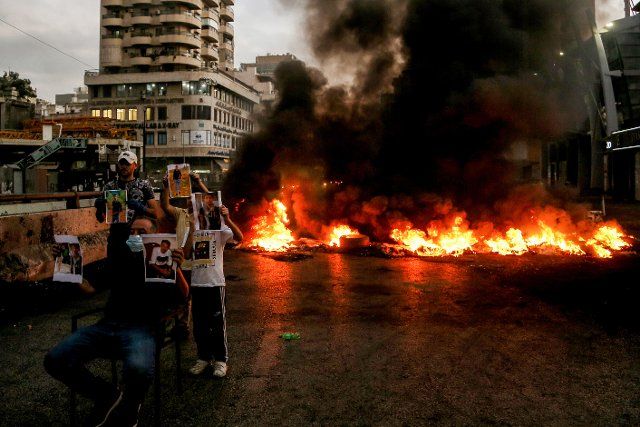 05 October 2022, Lebanon, Beirut: Relatives of detained individuals hold up their pictures in front of a black smoke wall billowing from burning tire blocking a highway in Beirut\