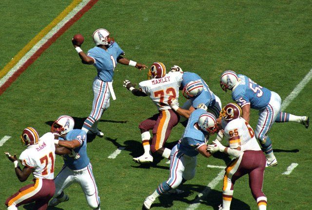 Houston Oilers quarterback Warren Moon (1) looks for a receiver during the game against the Washington Redskins at RFK Stadium in Washington, DC on September 16, 1985. Rushing Moon are Redskins defensive end Dexter Manley (72), defensive end Charles Mann (71), and defensive tackle Dave Butz (65). Among the linemen defending for Moon are Oilers right offensive tackle Bruce Matthews (74), right guard John Schuhmacher (62), offensive tackle Eric Moran (76), and center Jim Romano (55). The Redskins won the game 16 - 13 Credit: Howard L. Sachs \/ CNP