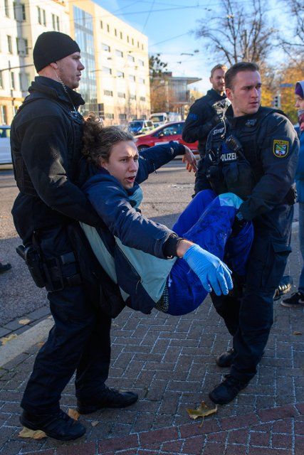21 November 2022, Sachen-Anhalt, Magdeburg: Police officers carry a "Last Generation" climate activist off the road. The activist had stuck one hand to the roadway during rush hour to protest the federal government\