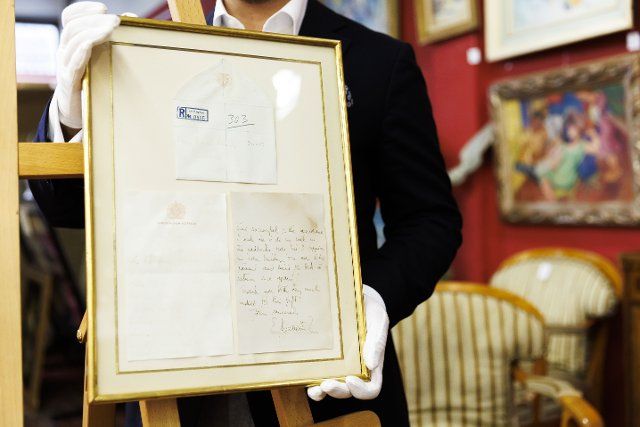 PRODUCTION - 25 November 2022, Baden-Wuerttemberg, Leinfelden-Echterdingen: The Stuttgart auction house Eppli auctions, in addition to other objects on the theme of "British royalty", a handwritten two-page letter from the recently deceased Queen Elizabeth II (1926-2022) from 1966 to a passionate equestrian. Ferdinand Eppli presents the object to be auctioned. It is the framed letter, a copy of the back and the envelope. Photo: Julian Rettig\/dpa