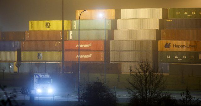 01 December 2022, Saxony, Leipzig: A truck waits in front of a wall of sea containers at the Leipzig-Wahren transhipment station in the early morning. The freight terminal went into operation in 2001. In 2017, an expansion with additional tracks and cranes doubled the facility\