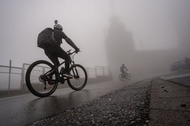 29 November 2022, Hessen, Schmitten: Two cyclists are on their way on the wet road to the summit plateau of the Großer Feldberg in Taunus, which is completely covered in fog. Photo: Frank Rumpenhorst\/dpa