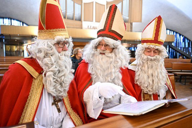 04 December 2022, Baden-Wuerttemberg, Friedrichshafen: Three members of the St. Nicholas Guild Friedrichshafen, dressed as St. Nicholas, sit during a service in the Catholic church "Zum guten Hirten", from where they are sent out. In the days leading up to the 4th of Advent, the guild visits around 150 families, clubs, kindergartens and care facilities. Photo: Felix Kästle\/dpa