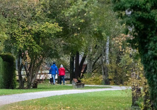 24 October 2018, Thuringia, Herrsching Am Ammersee: 24 October 2018, Germany, Herrsching Am Ammersee: Two people with dogs walk past a park bench in the Kurpark. Photo: Lino Mirgeler\/