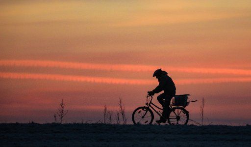 13 February 2019, Baden-Wuerttemberg, Riedlingen: A cyclist is in minus degrees before the red colored morning sky on the way. Photo: Thomas Warnack\/
