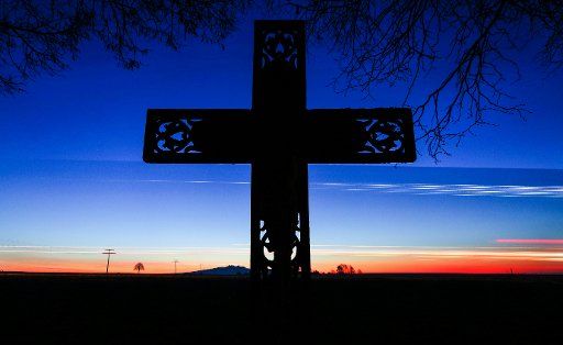 15 February 2019, Baden-Wuerttemberg, Daugendorf: A cross stands at sunrise on the Bundesstraße 312. The lights of passing cars and trucks leave streaks. (Shooting with long exposure) Photo: Thomas Warnack\/