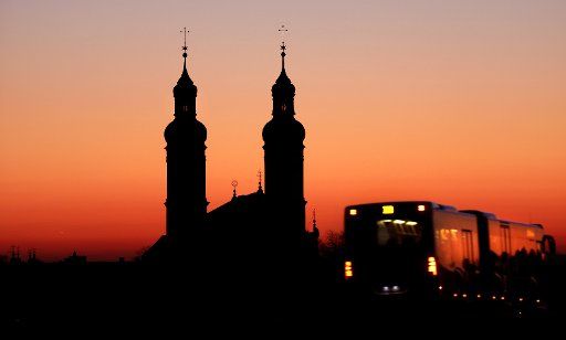 24 February 2019, Baden-Wuerttemberg, Obermarchtal: Shortly before sunrise, a bus passes the towers of St. Peter and Paul\
