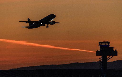 21 March 2019, Hessen, Frankfurt\/Main: A passenger aircraft takes off in the last light of the setting sun over the tower of the airport, while the sky glows red. The weather should remain clear and spring-like in the coming days. Photo: Boris Roessler\/