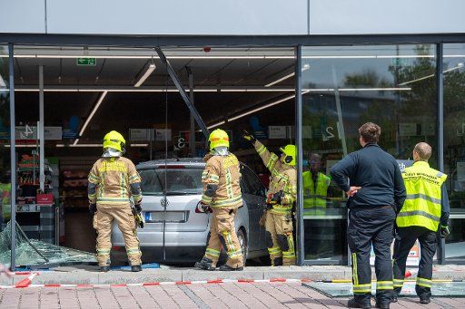 07 May 2019, Bavaria, Munich: Firefighters cut a car out of the glass front of a supermarket. Photo: Lino Mirgeler\/dpa - ATTENTION: The car license plate was pixelated for legal