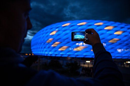 09 May 2019, Bavaria, Munich: A man takes a picture of the Allianz Arena, which lights up in the colours of the flag of the European Union on Europe Day. Photo: Sina Schuldt\/