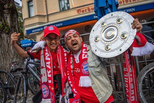 18 May 2019, Bavaria, Munich: Ahmed Haidar and his daughter Lisa hold a championship bowl in their hands and celebrate the German Football Championship of FC Bayern Munich on Leopoldstraße. Photo: Lino Mirgeler\/