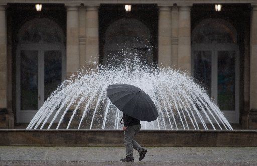 21 May 2019, Baden-Wuerttemberg, Stuttgart: A man with a large umbrella walks across the forecourt of the New Palace in front of a fountain. Photo: Marijan Murat\/