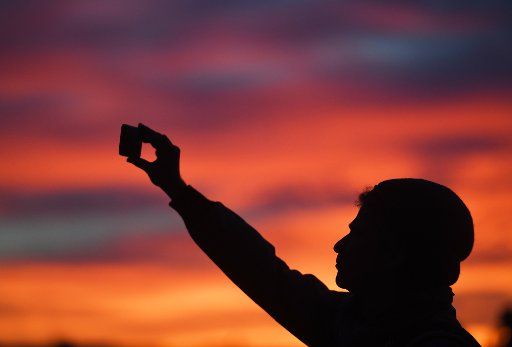 A man takes a picture of the colourful evening sky with his smartphone in Freiburg, Germany, 28 October 2017. Photo: Patrick Seeger\/
