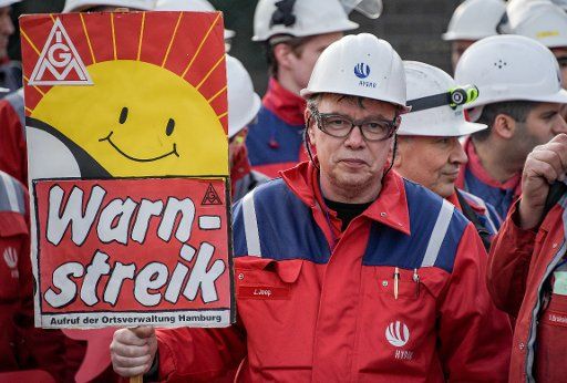 Hydro Aluminium workers standing in front of the factory gates holding in his hands a sign with the text "warning strike" during a rally part of a warning strike by IG Metall workers in Hamburg, Germany, 10 January 2018. Photo: Axel Heimken\/