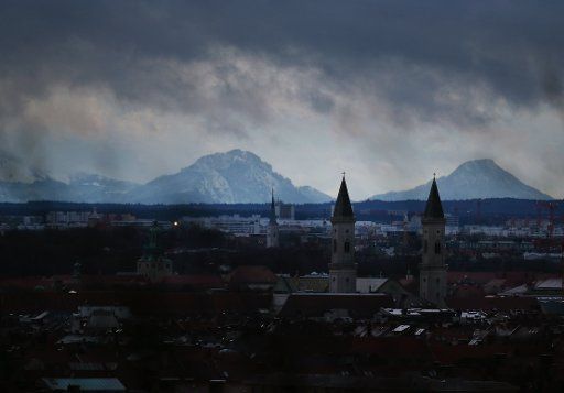 dpatop - Dark snow clouds move above Munich, as seen from the Olympiaberg in Munich, Germany, 17 January 2018. The church St. Louis can be seen in front of the mountains. Photo: Lisa Forster\/