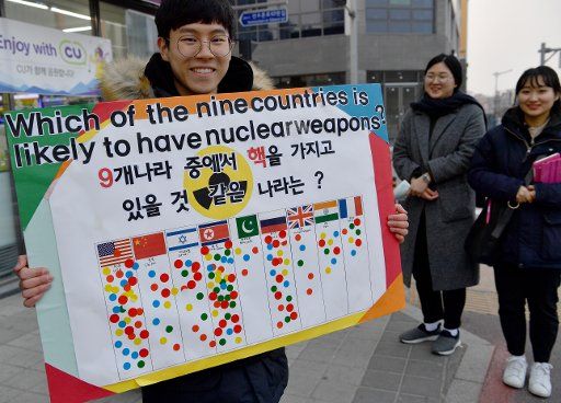 22 February 2018, South Korea, Gangneung, Winter Olympics, Olympic Village: A protestor carries a sign which depicts the probabilities of owning nuclear weapons for specific countries near the Olympic village. Photo: Peter Kneffel\/